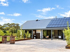 Ein Haus mit überdachter Terrasse, Solaranlage auf dem Dach und Auffahrt mit Kies.