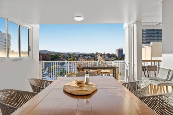 Ein Balkon mit Holztisch, Korbstühlen und Blick auf die Stadt.