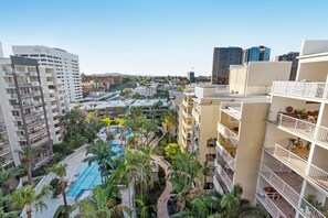 Ein Hochhaus-Hotel mit zahlreichen Balkonen, einem von Palmen umgebenen Swimmingpool und Blick auf die Skyline.