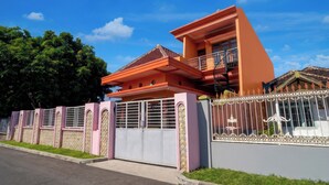 Una casa de dos pisos con balcón, entrada protegida por un portón y césped bien cuidado.