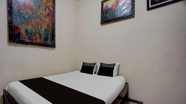 A bedroom with a bed, two pillows, and two wall-mounted paintings.