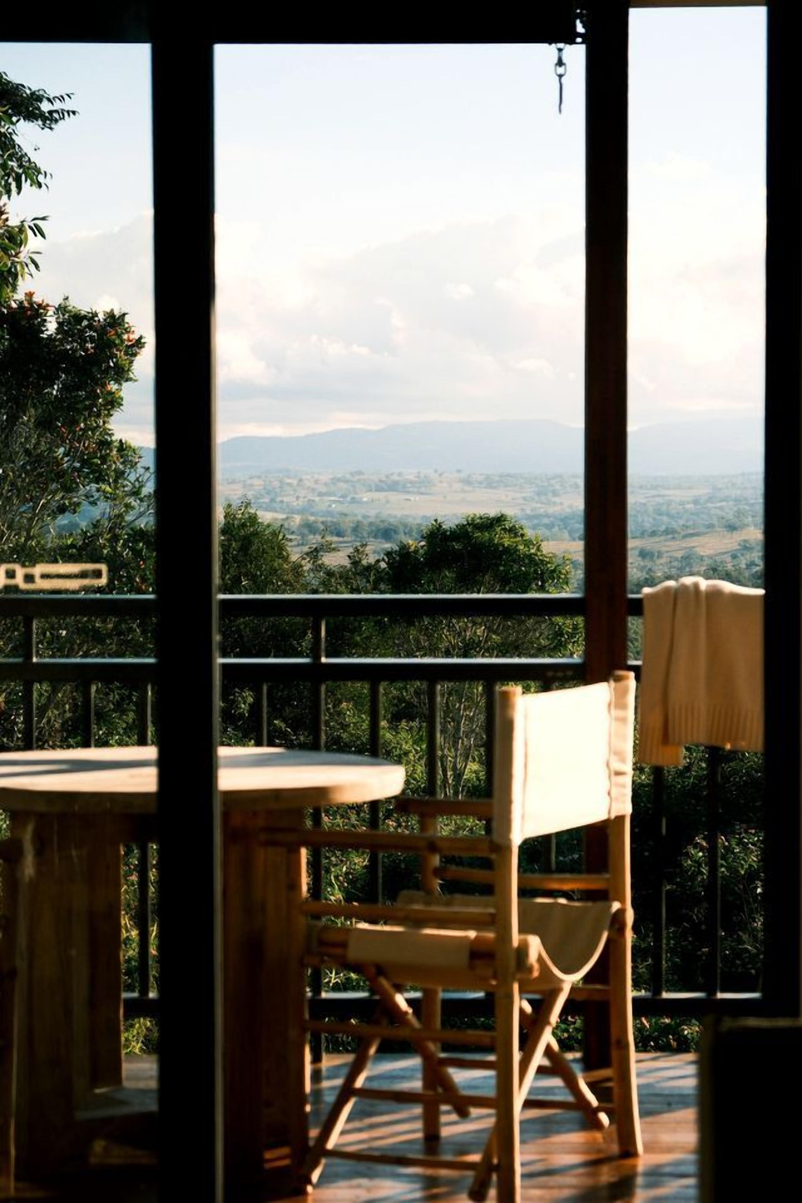 A wooden chair and table on a balcony with a view of a landscape.