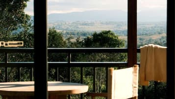 A wooden chair and table on a balcony with a view of a landscape.