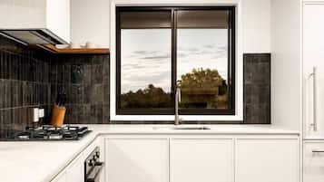 Eine moderne Küche mit weißen Schränken, einem großen Fenster und Blick ins Freie.