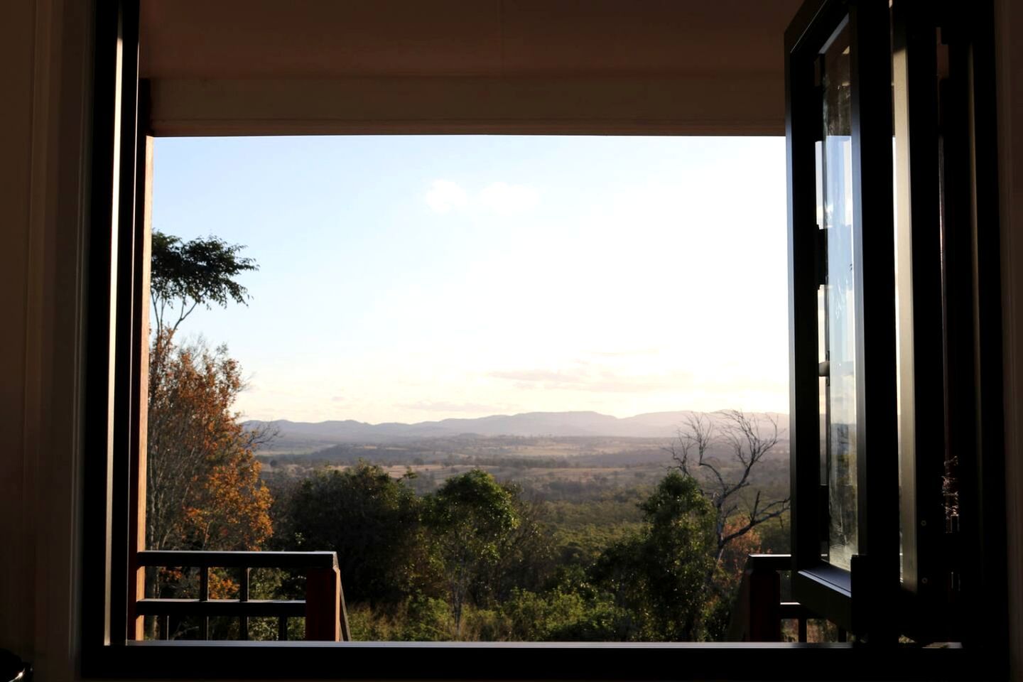 Une vue depuis une fenêtre donnant sur un paysage, avec des arbres et des collines au loin.