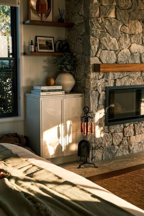 A bedroom with a stone wall, a fireplace, a bed, and a window with daylight.