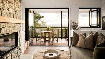 A living room with a stone wall, a fireplace, a round coffee table, a sofa, and a balcony with a table and chairs.