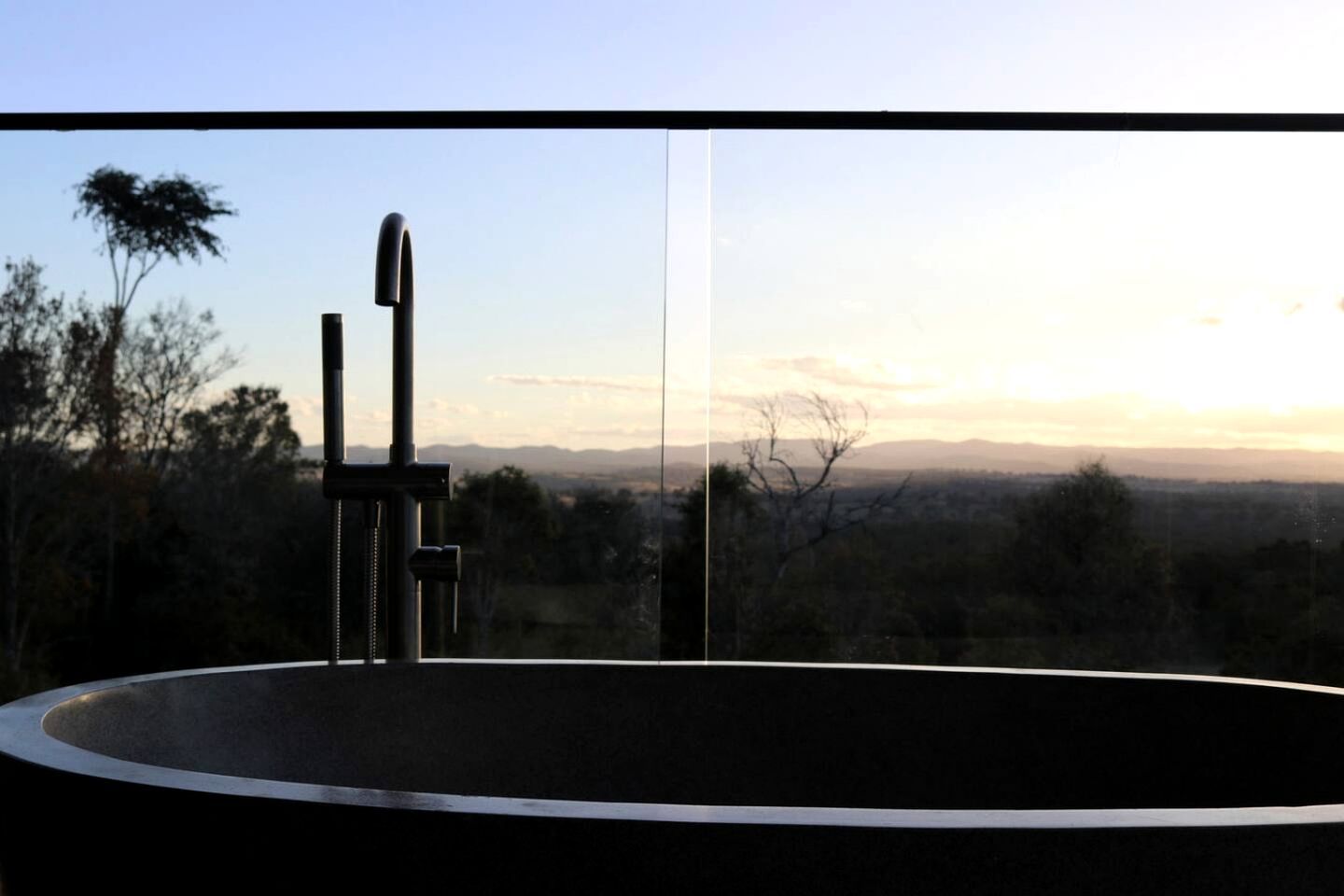 A circular pool with a modern faucet, surrounded by a balcony with a view of a distant landscape.