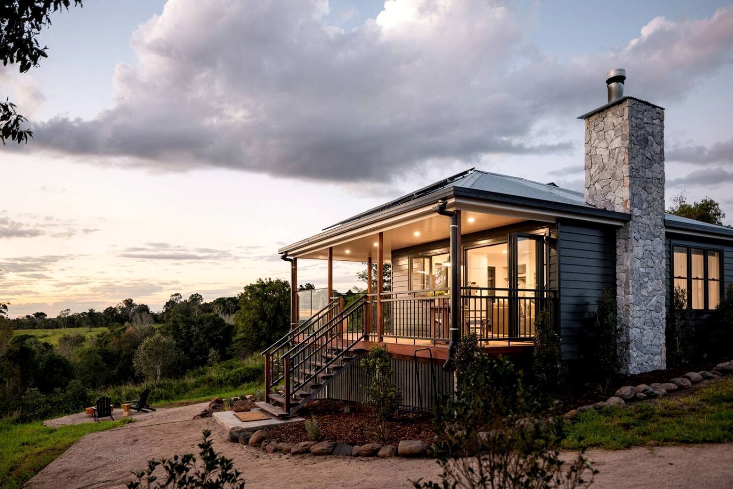 Une maison moderne avec une cheminée en pierre, une véranda et une vue sur le paysage environnant.