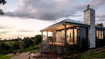Une maison moderne avec une cheminée en pierre, une véranda et une vue sur le paysage environnant.