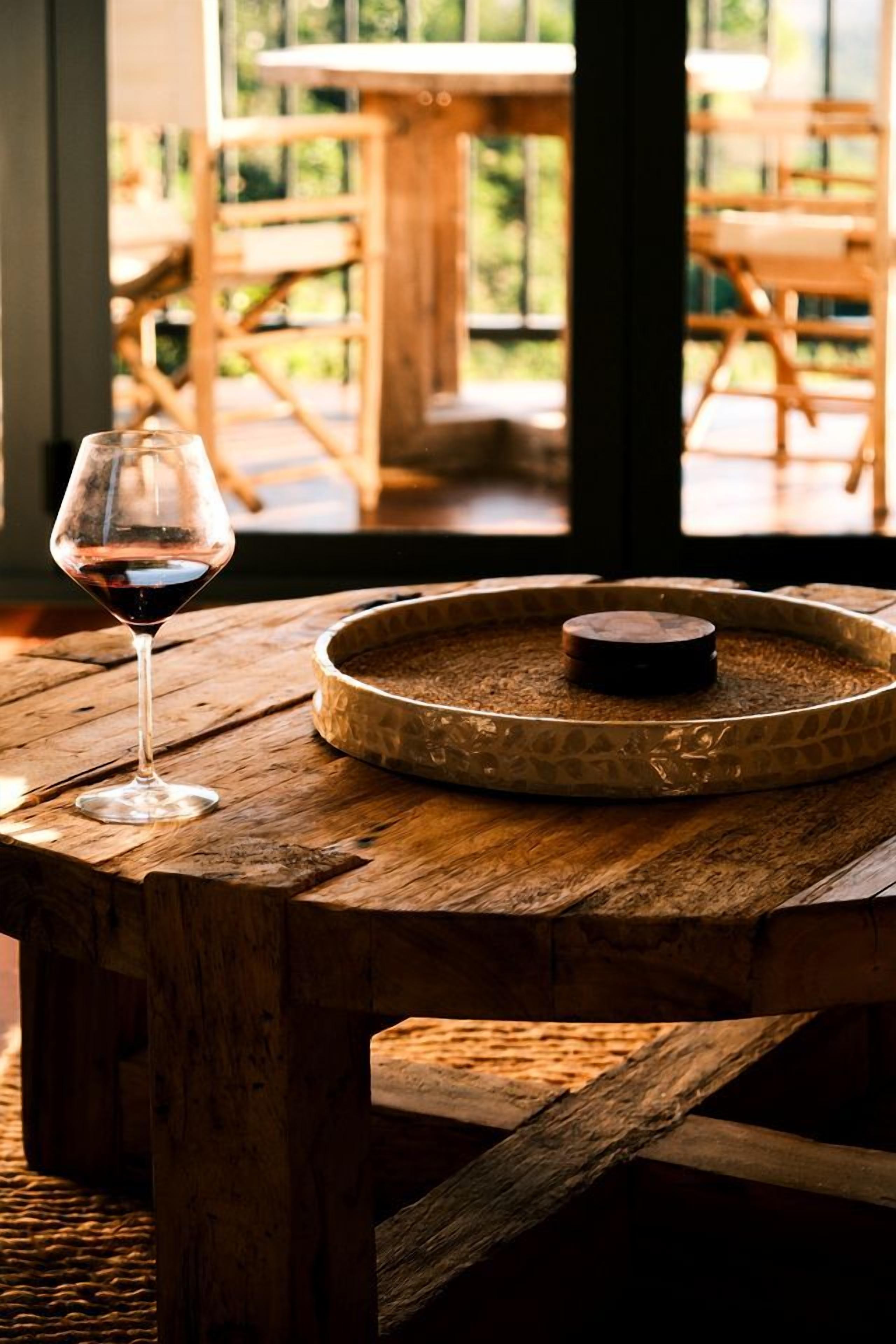 Ein rustikaler Holztisch mit einem Glas Rotwein und einer runden Platte mit einer Kerze.