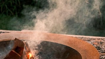 A circular metal fire pit with burning logs and smoke.