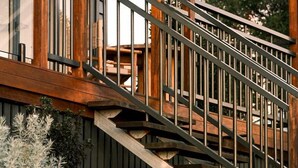 A wooden staircase with metal railings leading to a covered outdoor area.