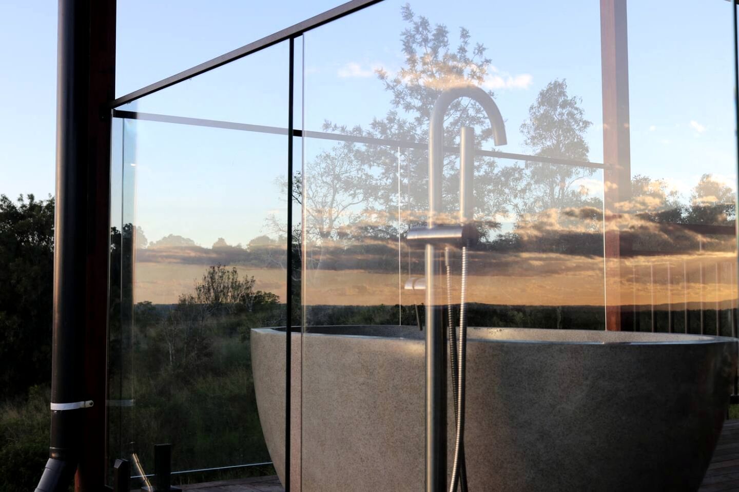 A modern bathroom with a large bathtub, a faucet, and a view of a natural landscape through large windows.