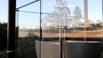 A modern bathroom with a large bathtub, a faucet, and a view of a natural landscape through large windows.