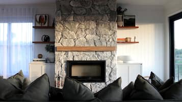 Ein Wohnzimmer mit Kamin aus Stein, einem Flachbildfernseher, einer Couch mit Kissen und einem großen Fenster.