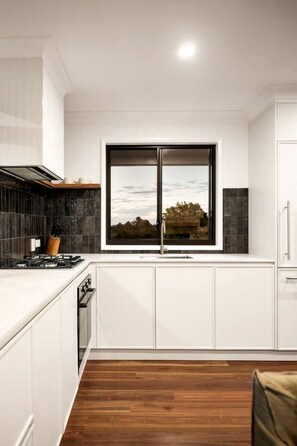 A modern kitchen with white cabinetry, a large window, and a view of the outdoors.