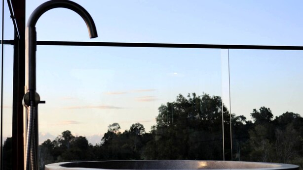 A bathroom with a large sink, a faucet, and a view of trees and sky.