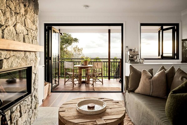 A living room with a stone wall, a fireplace, a round coffee table, a sofa, and a balcony with a table and chairs.