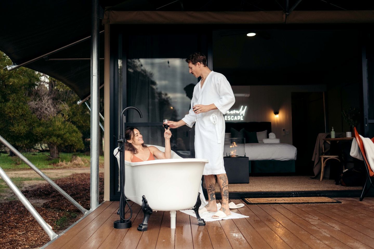 A person in a bathtub with a man standing beside them, holding a glass.