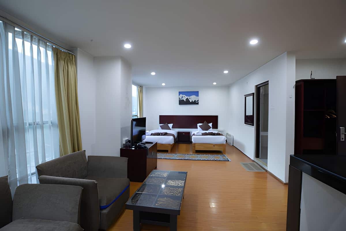 A hotel room with two beds, a sofa, a TV, and a painting on the wall.