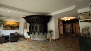 Eine Lobby mit einer Rezeption, einer Couch, einer Topfpflanze, einem Gemälde und einer Steinwand.