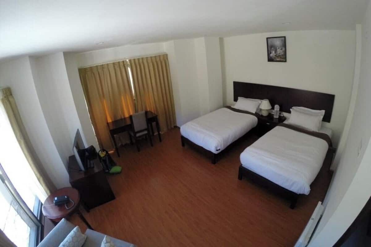A hotel room with two beds, a desk, a chair, a TV, and a window with curtains.