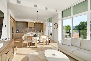 A modern kitchen with a dining area, large windows, and a view of greenery.