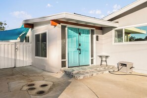 Een huis met een turquoise deur, een klein terras, een witte hekken en een raam met uitzicht.