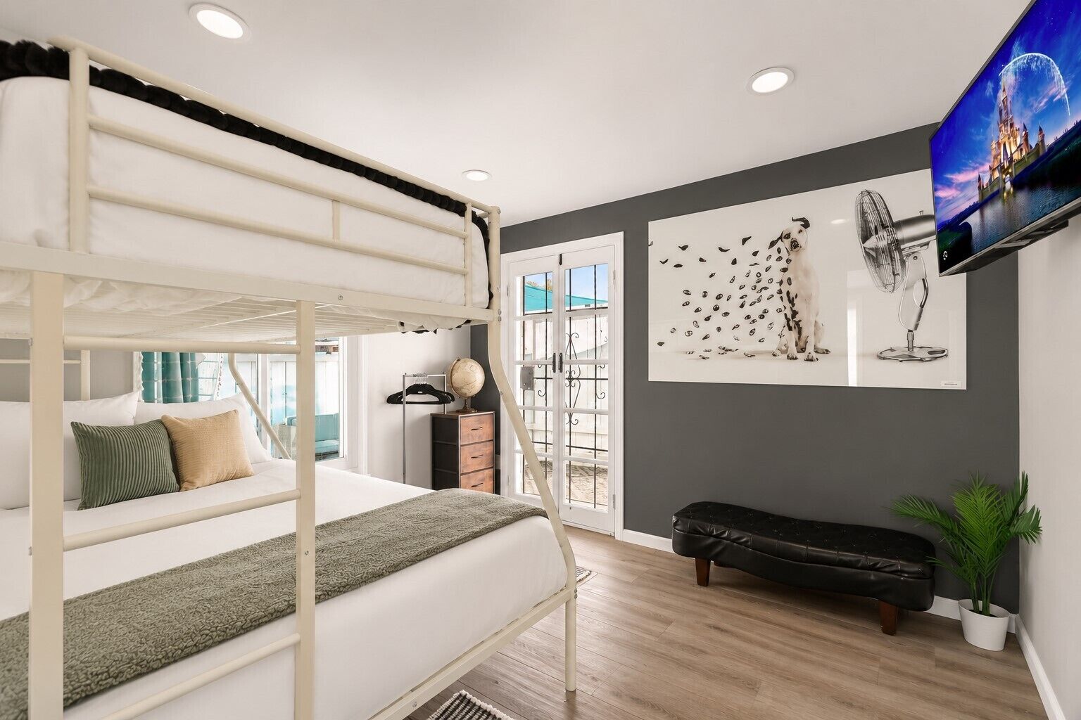 Ein Stockbett mit Schreibtisch und Globus, eine schwarze Lederbank, ein Blumentopf und ein Fernseher an der Wand.