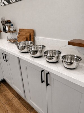 Uma bancada de cozinha com tigelas de aço inoxidável, tábua de corte de madeira e porta-facas.