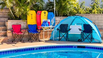 A poolside area with a tent, two chairs, a cooler, and surfboards.