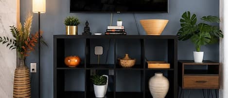 A living room with a flat-screen TV mounted on the wall, a black entertainment unit below, a wooden coffee table, and a patterned rug.
