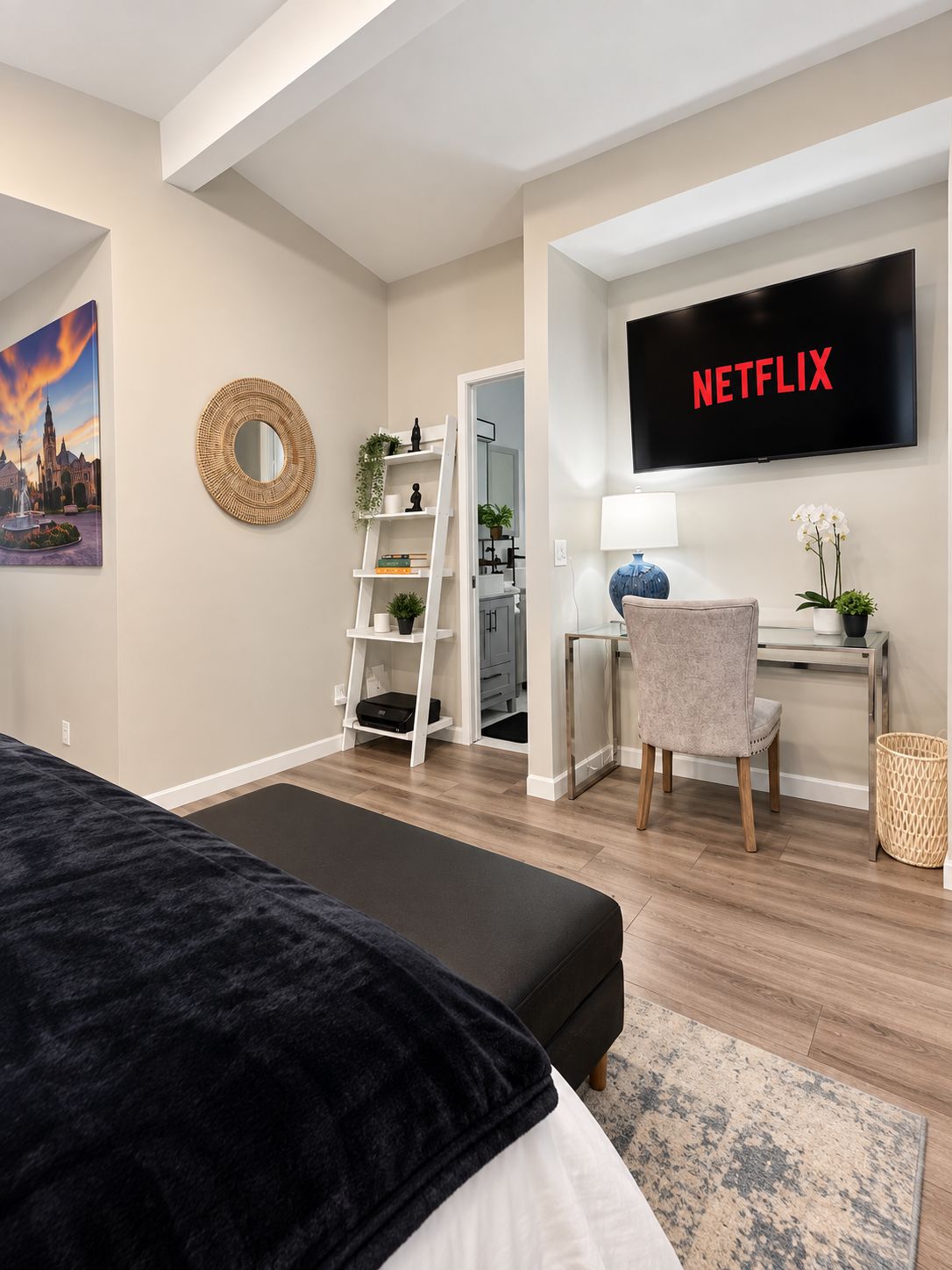 A bedroom with a bed, a desk with a chair, a TV mounted on the wall, and a bookshelf.
