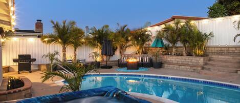 A backyard with a swimming pool, hot tub, barbecue grill, and outdoor seating area.