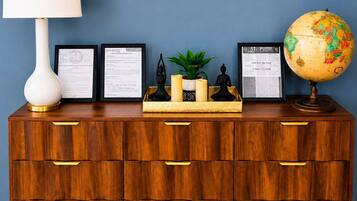 A wooden dresser with multiple drawers, a white lamp, framed certificates, a small plant, candles, and a globe.