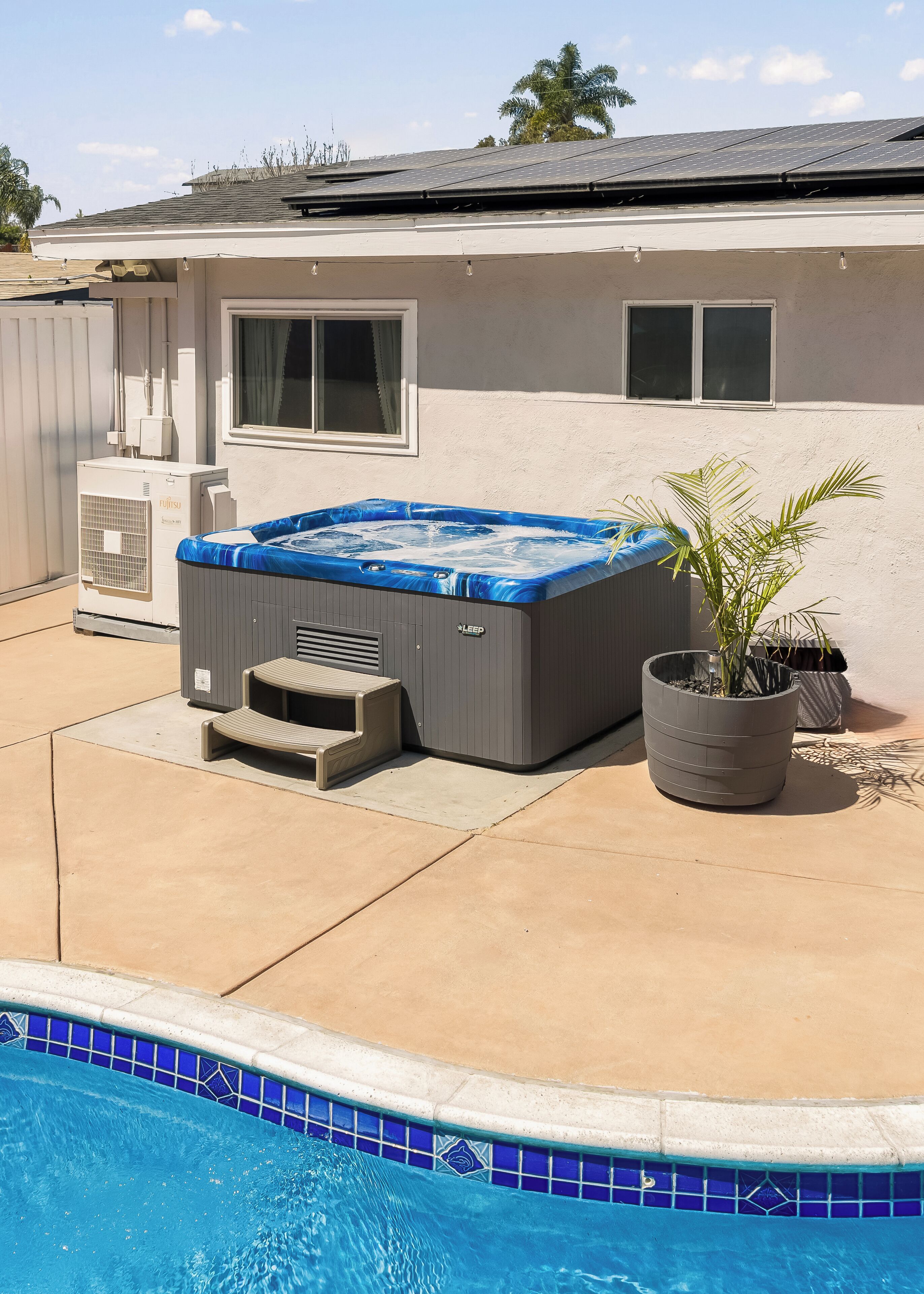 Ein Whirlpool mit Stufen, ein Pool mit blauen Fliesen und ein Haus mit weißer Fassade.