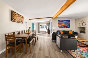 Een moderne woonkamer met een eethoek, een zithoek, een schilderij en een houten balk.