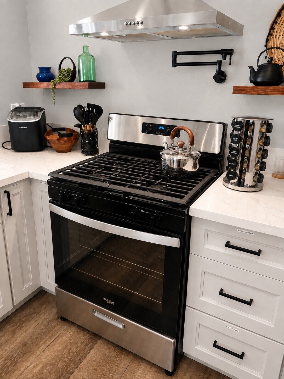 Una cocina con estufa integrada, horno y campana extractora encima. Hay armarios, un tostador y un hervidor en la encimera.