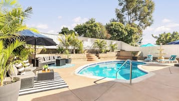 A swimming pool with a sunken seating area, surrounded by lounge chairs and umbrellas.