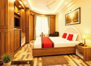 Una habitación de hotel con una cama grande, un ventilador de techo, un cuadro en la pared y una mesita con una lámpara.
