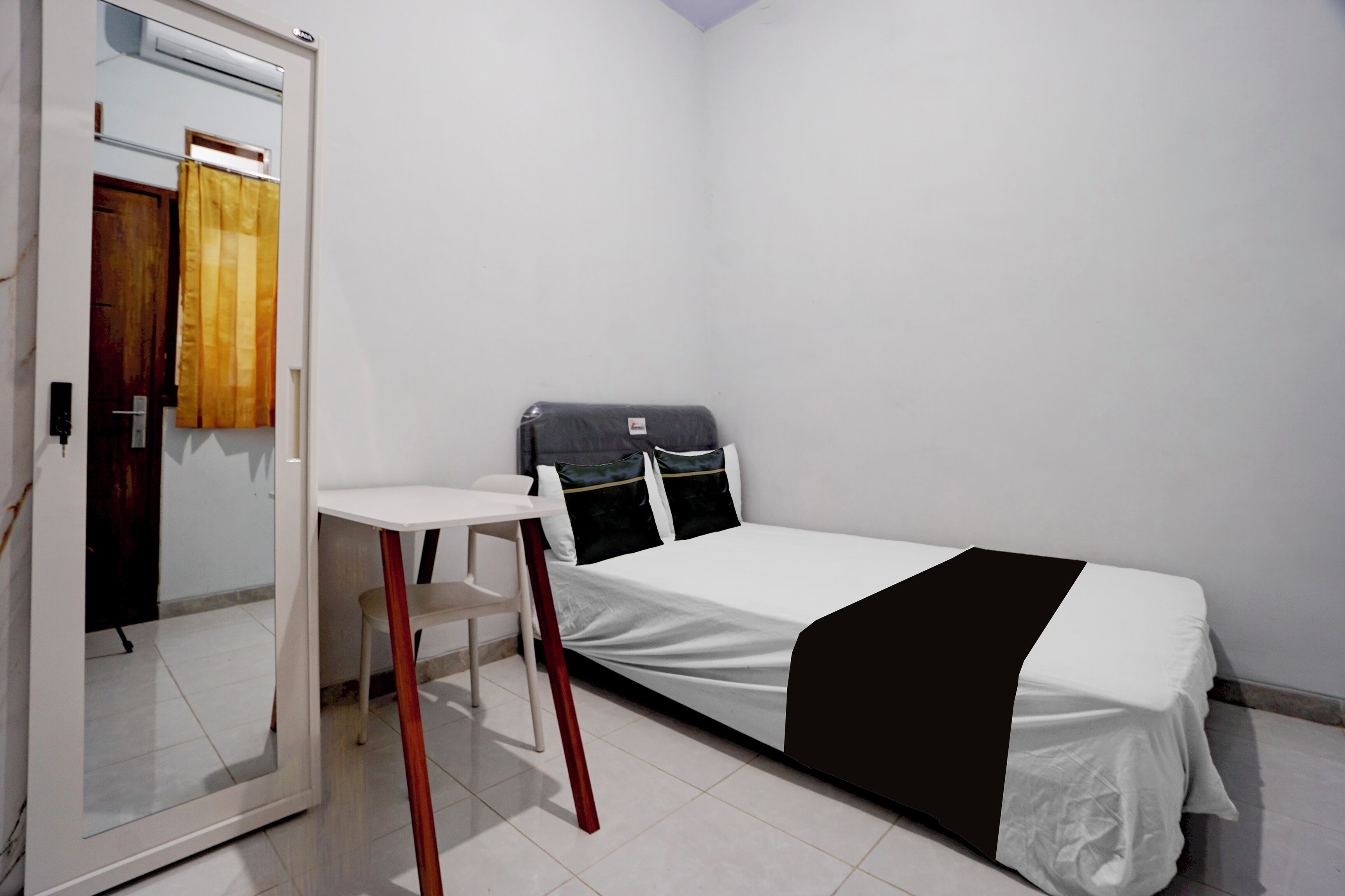 Um quarto pequeno e limpo com uma cama, uma escrivaninha e uma cadeira.