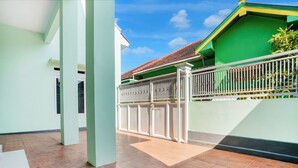 A spacious outdoor area with a tiled floor, a white fence, and a green building with a red roof. - OYO 95293 Citra Homestay Syariah (Pasuruan)