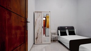 A hotel room with a wooden door, a marble-framed mirror, a white chair, a bed with a black headboard, and a tiled floor. - OYO 95293 Citra Homestay Syariah (Pasuruan)