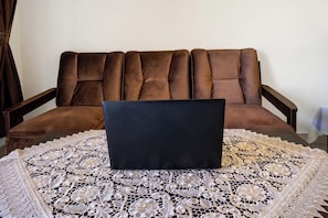 Un ordinateur portable posé sur une table recouverte d’une nappe en dentelle, un canapé marron et un rideau dans une pièce.