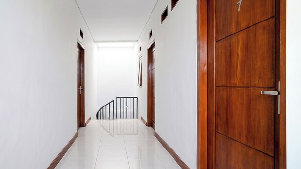 A hallway with white walls, wooden doors, and a tiled floor. - OYO 95293 Citra Homestay Syariah (Pasuruan)