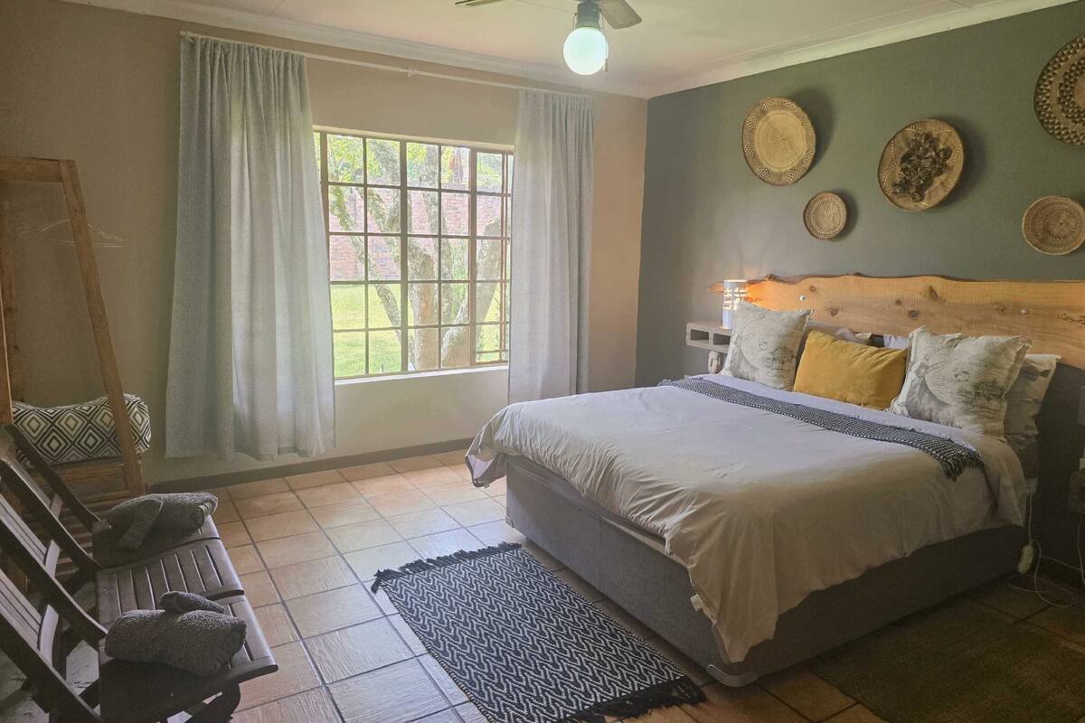 A bedroom with a bed, a ceiling fan, a window with curtains, a wooden headboard, and wall decorations.