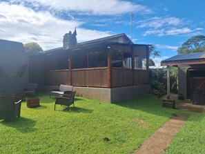 Ein Haus mit einer Holzterrasse, einem Steinkamin und einem umzäunten Garten.