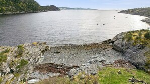 Un paisaje costero con costa rocosa, mar tranquilo y colinas a lo lejos.