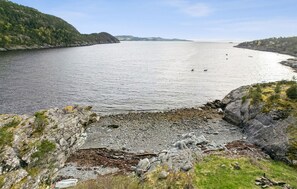 Eine Küstenlandschaft mit felsiger Küste, ruhiger See und fernen Hügeln.